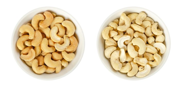 Cashew nuts in white porcelain bowls. Raw and processed nuts. Whole, roughly chopped, roasted, salted and as butter. Anacardium occidentale. Seeds. Isolated food photo, close up from above over white.